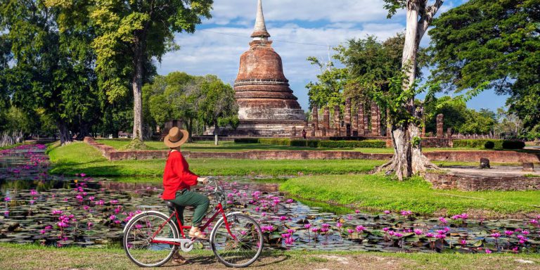 Femme à vélo près d'un temple en Thaïlande.